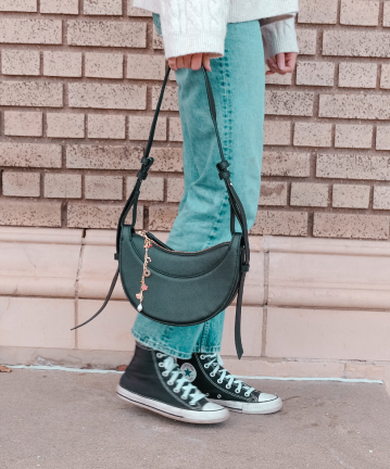 Stylish bag with dangly charm attached, featuring colorful heart and lucky clover details, paired with casual jeans and sneakers for a trendy look.